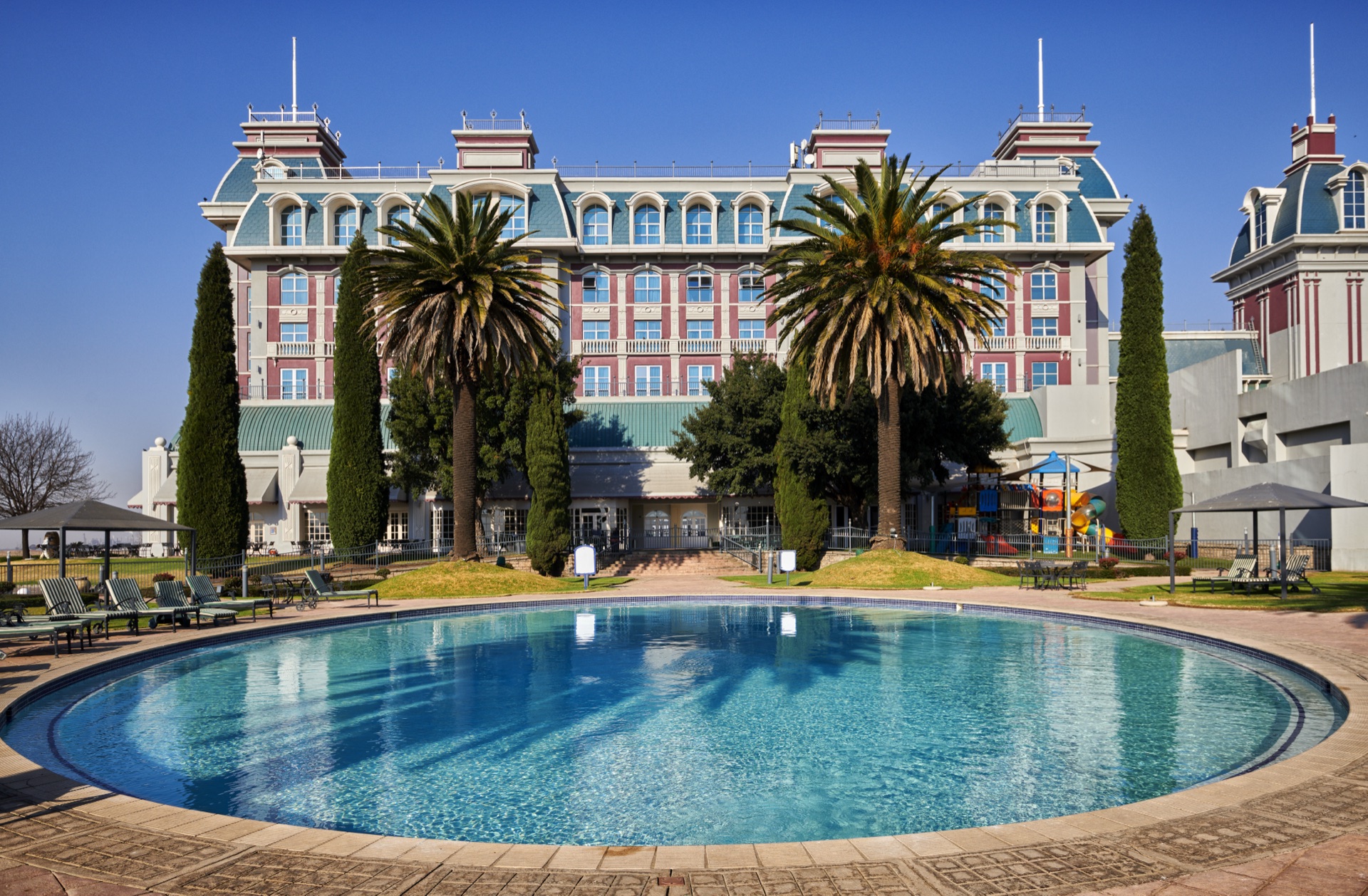 Circular outdoor swimming pool below the hotel and palm trees at Graceland, Secunda