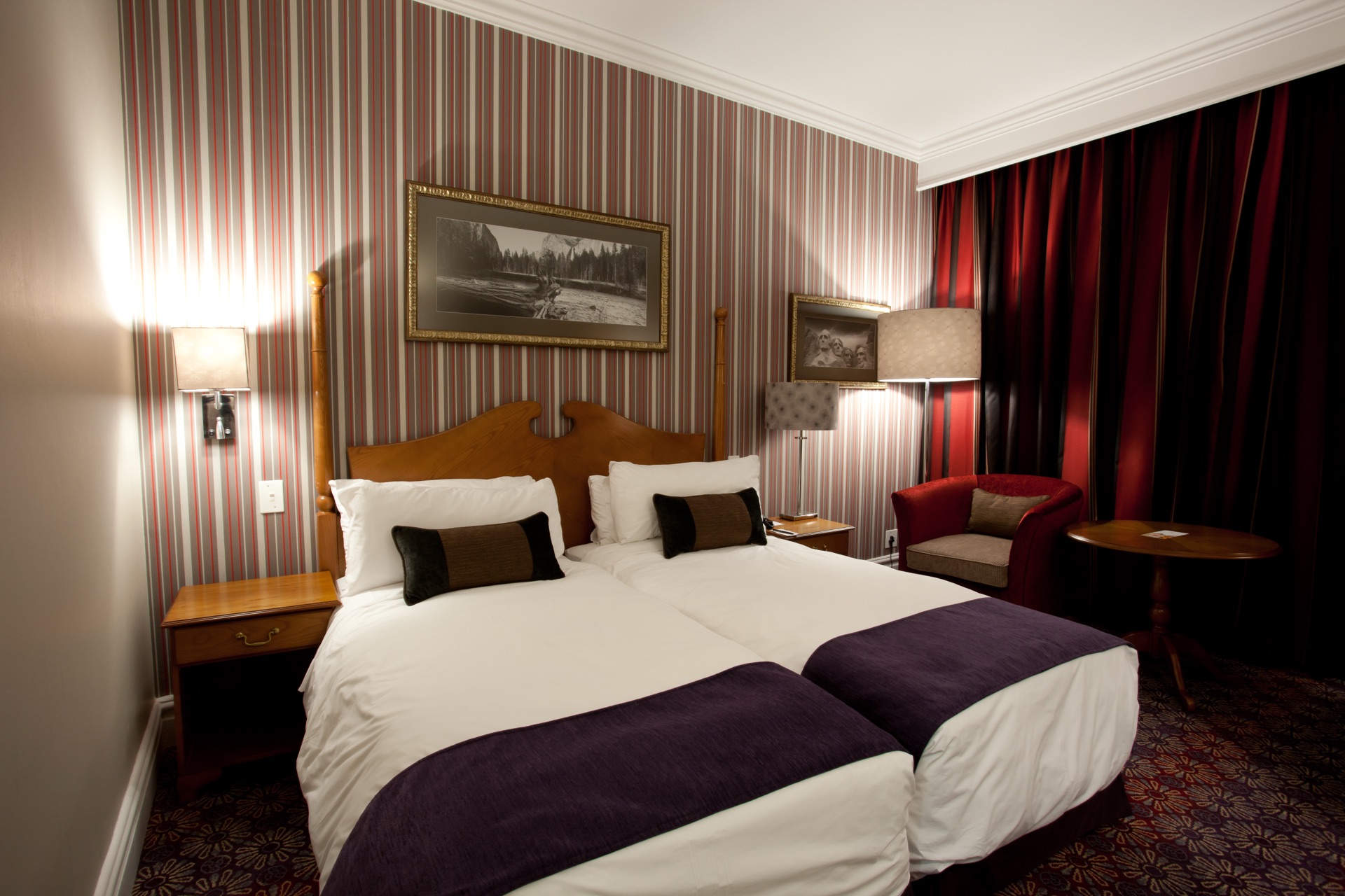 Classic Twin Room with striped walls, twin beds and red armchair at Walmont Hotel at Graceland, Secunda
